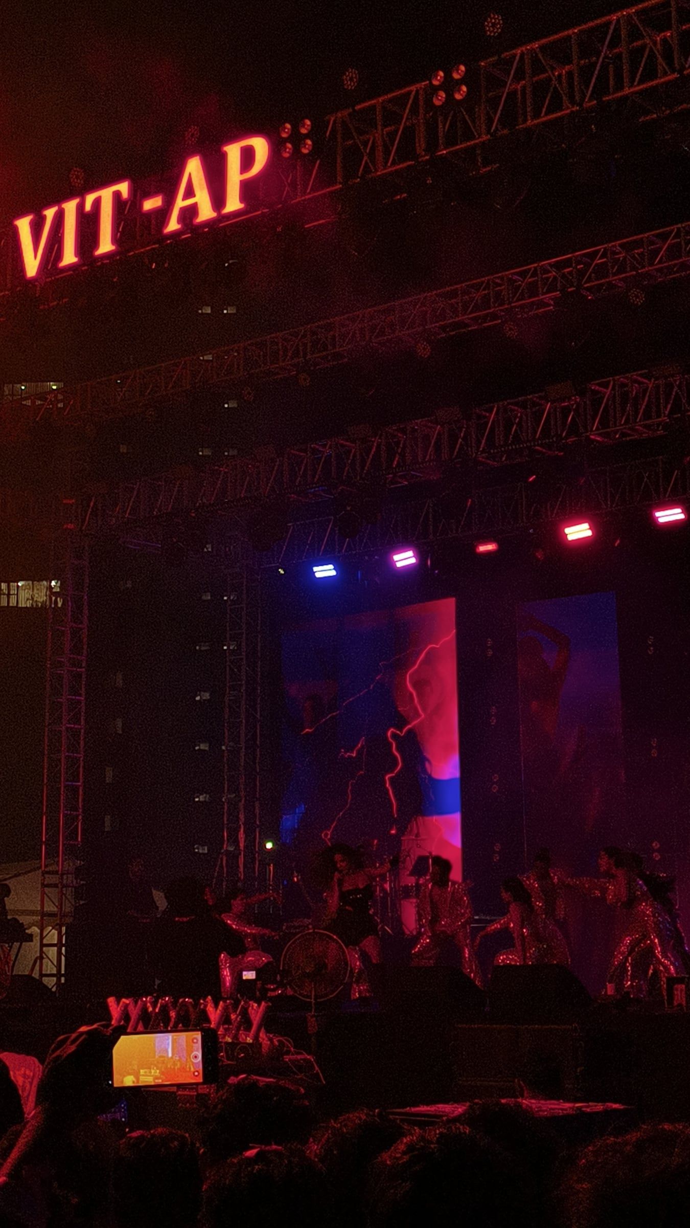 A crowd in front of a lit stage with a red VIT-AP sign at night