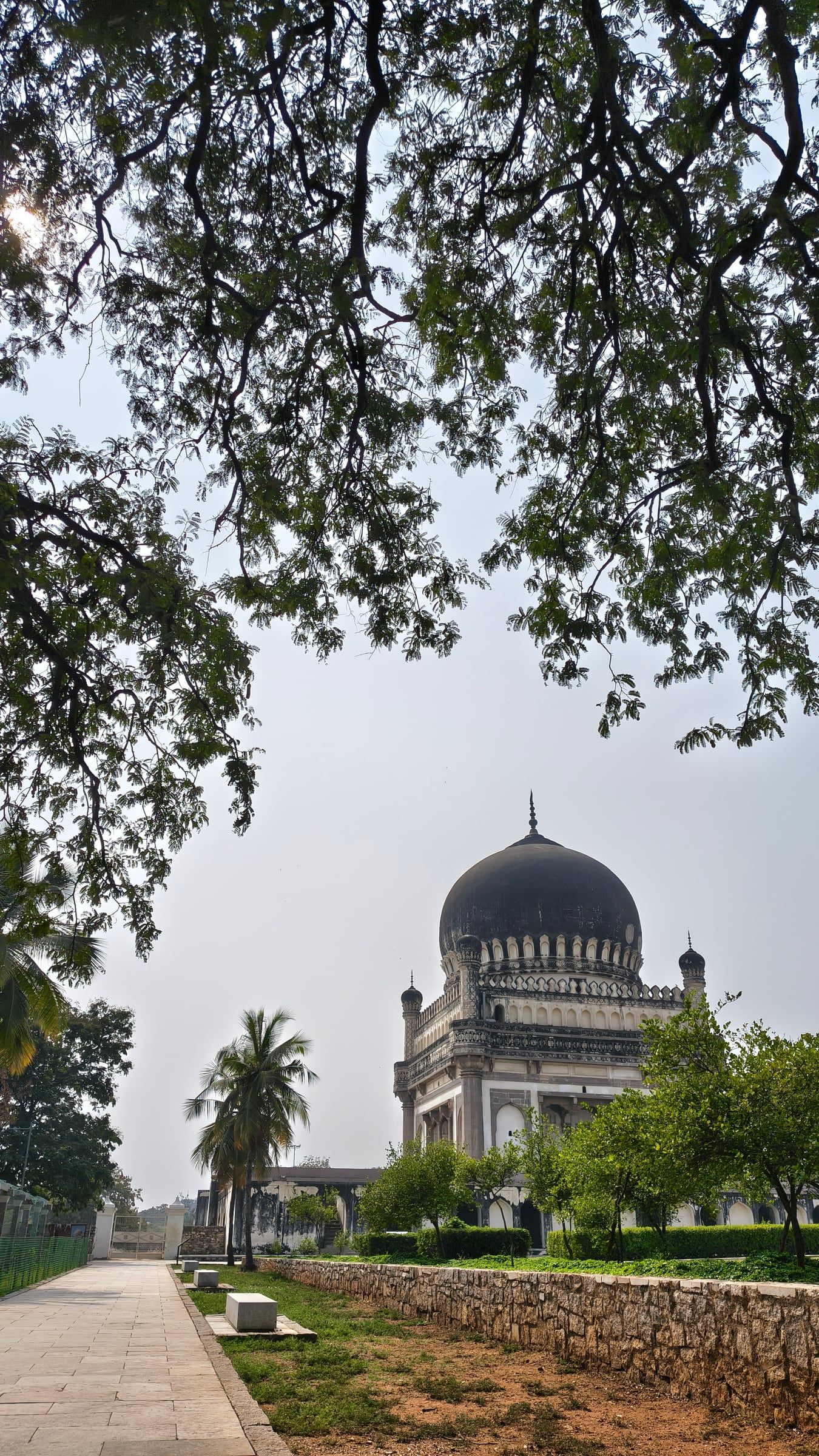 A domed tomb seen at the end of a path, framed by tree branches