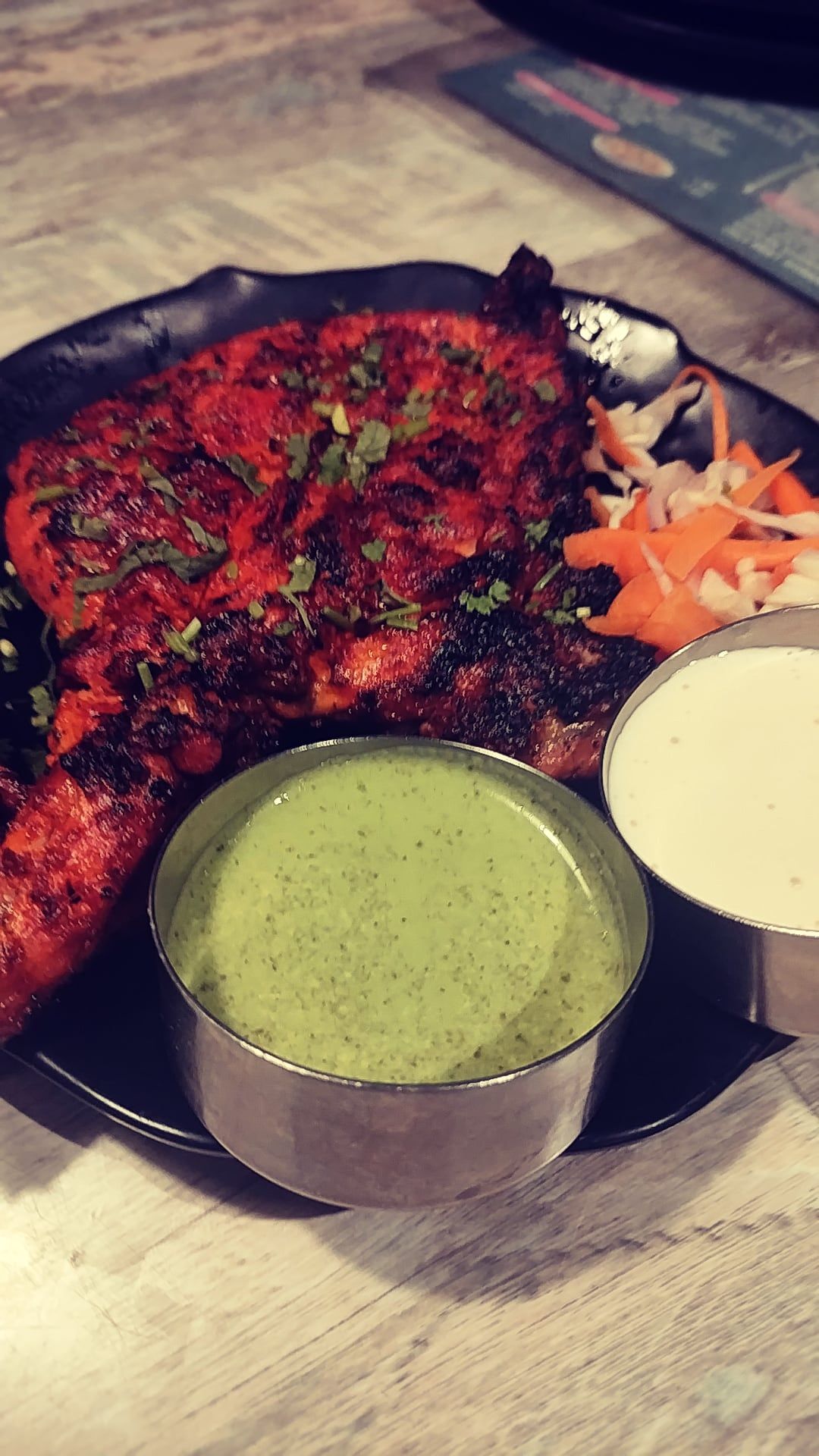 A plate of grilled food with two small bowls of chutney